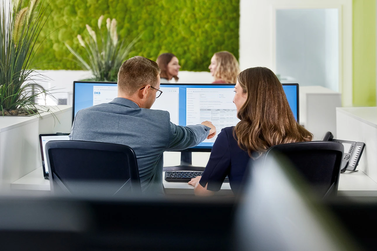 Im Großraumbüro schauen Personen gemeinsam auf einen Monitor