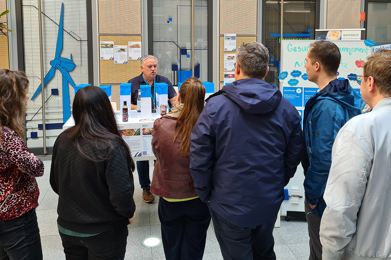 8 Personen stehen im DKB Atrium um einen Tisch mit zuckerhaltigen Lebensmitteln