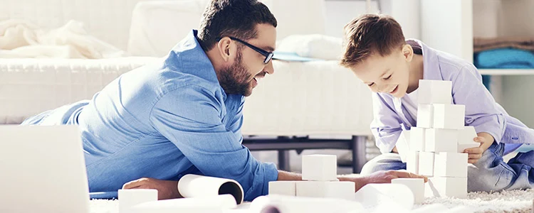 Vater und Sohn spielen mit weißen Bauklötzen auf einem weißen Wohnzimmerteppich vor einem weißen Sofa.