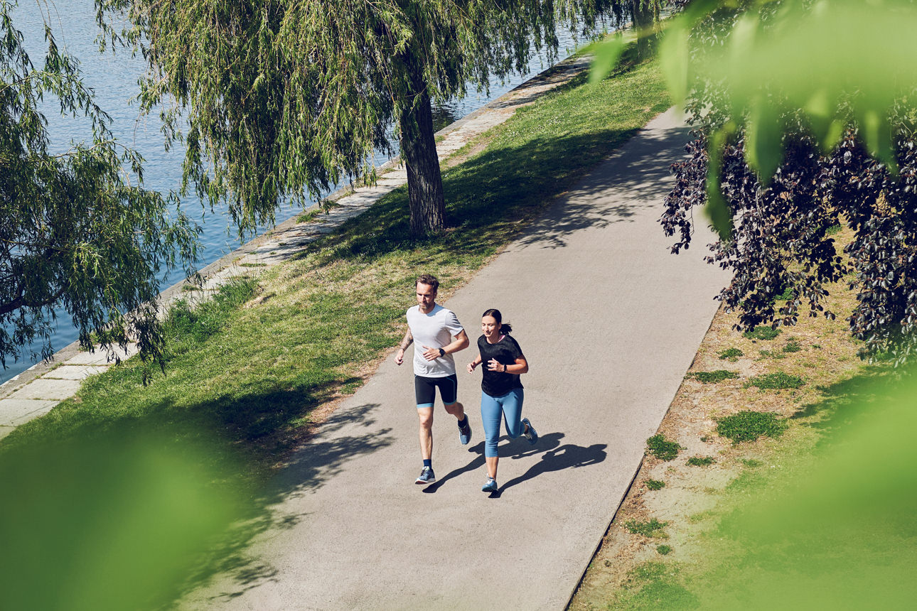 Zwei Personen joggen an einem Flussufer entlang