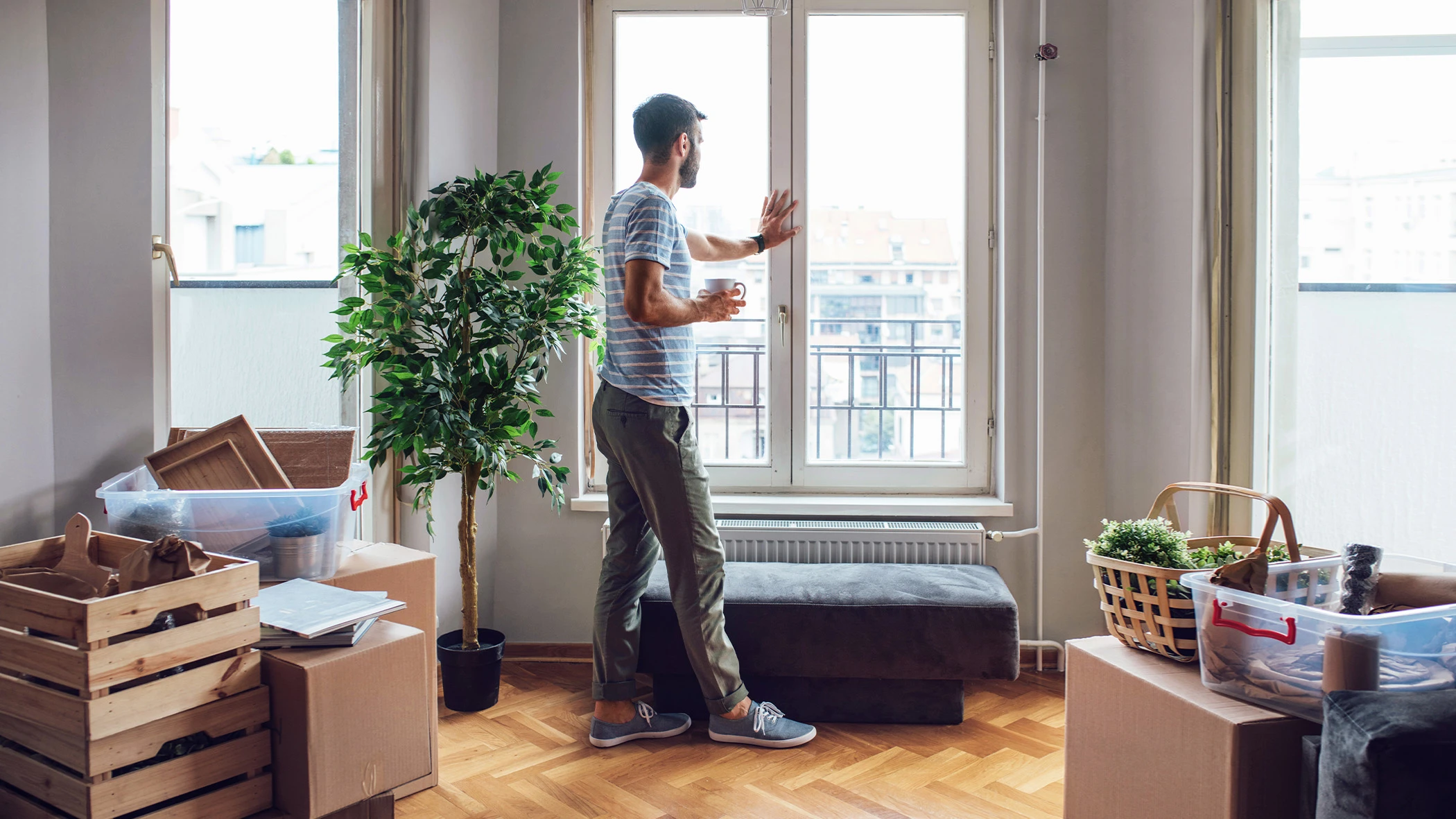 Ein Mann mit Kaffeetasse steht am Fenster einer neu bezogenen Wohnung.