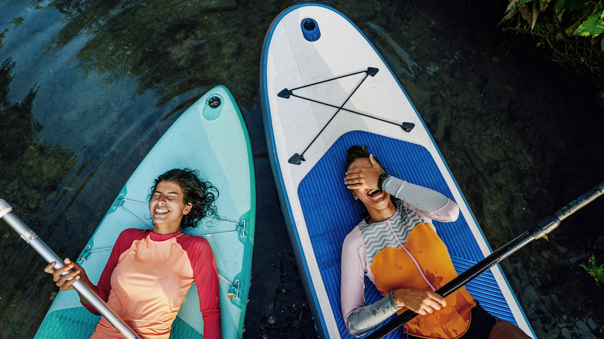 Zwei Frauen liegen auf Stand-up-Paddle-Boards und lachen.