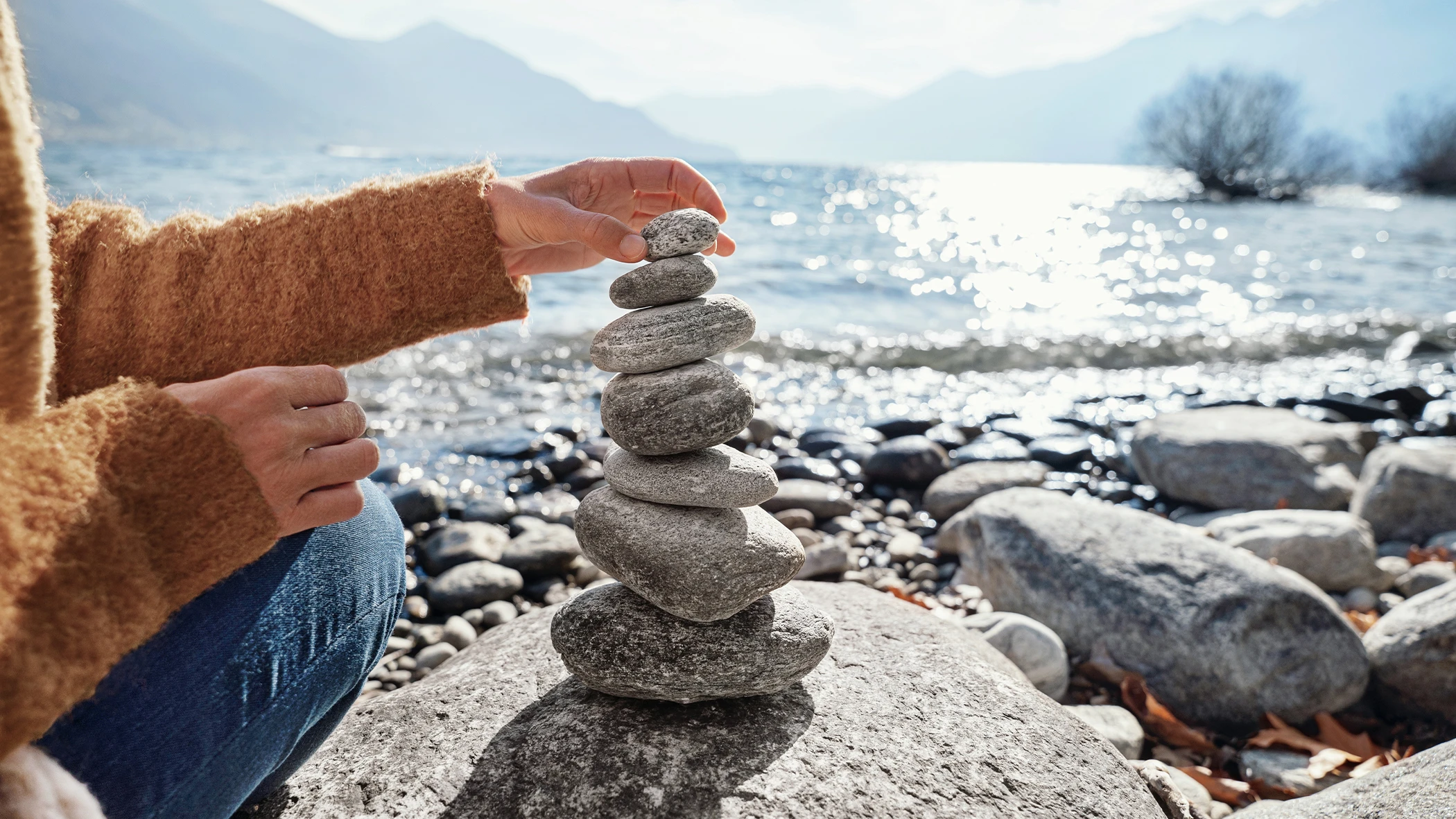 Eine Hand baut einen Turm aus Steinen vor einem See.