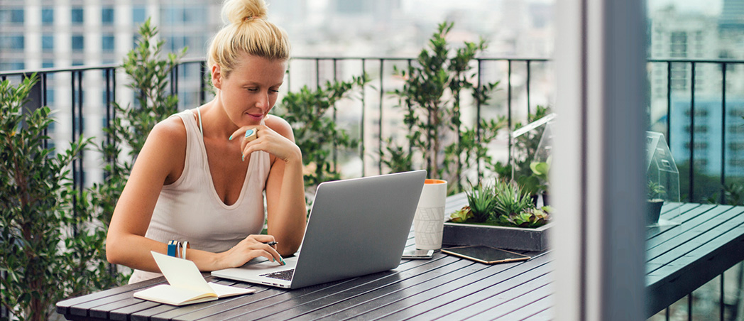 Eine Frau sitzt auf dem Balkon und arbeitet an einem Laptop