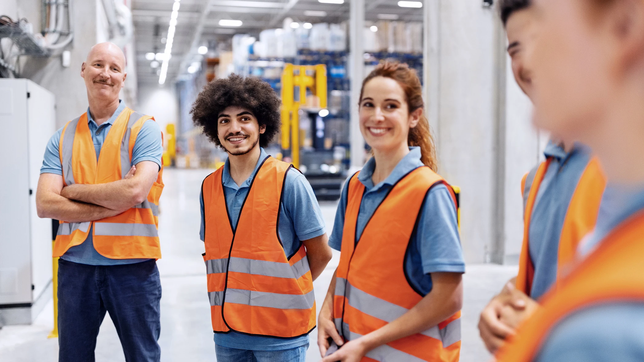 Eine diverse Gruppe von Personen in Schutzwesten stehen in einer Fabrik.