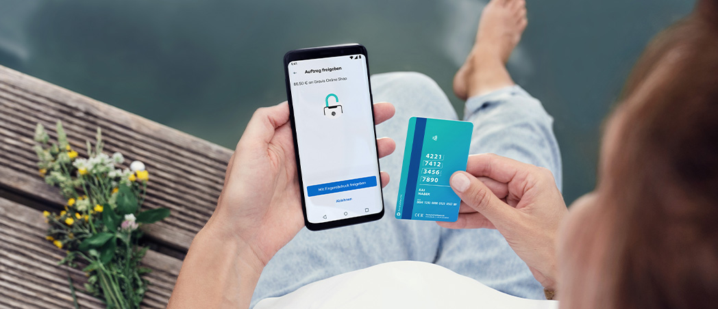 Person hält Visa Debitkarte, gibt Auftrag in DKB App frei