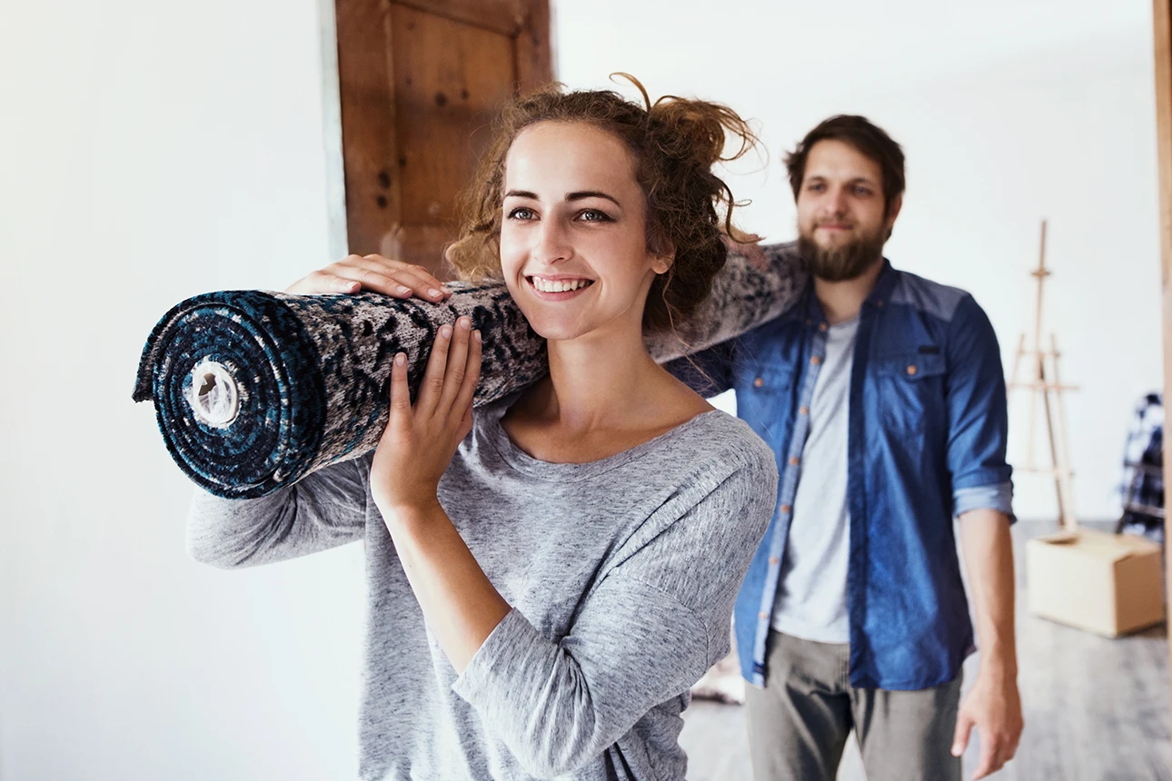 Eine Frau und ein Mann tragen gemeinsam einen Teppich in eine neue Wohnung