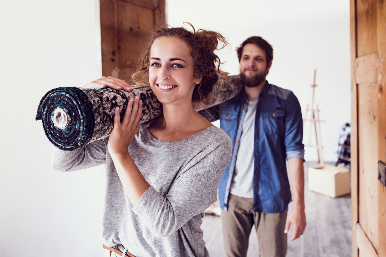 Eine Frau und ein Mann tragen gemeinsam einen Teppich in eine neue Wohnung.