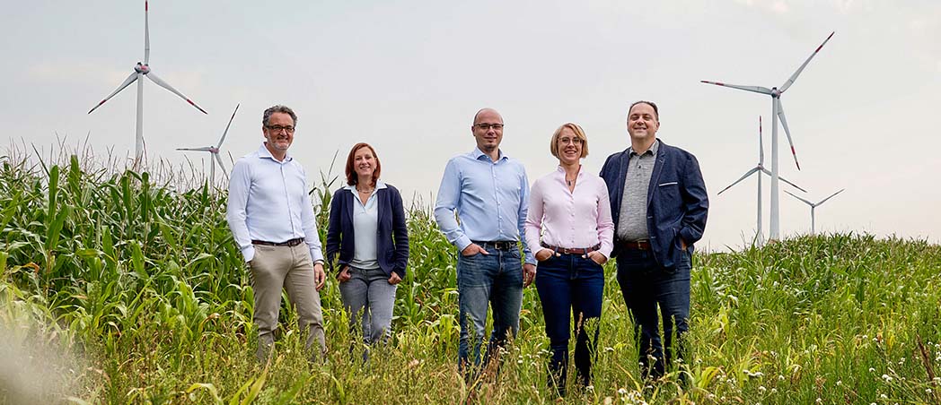 Eine Gruppe steht auf einem Feld mit Windrädern im Hintergrund