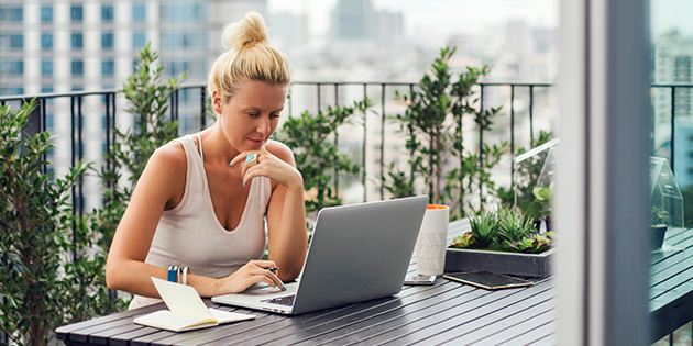 Eine Frau sitzt auf dem Balkon und arbeitet an einem Laptop.