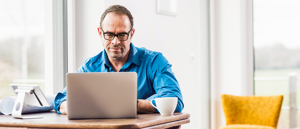 Ein Mann sitzt am Schreibtisch und arbeitet an einem Laptop.