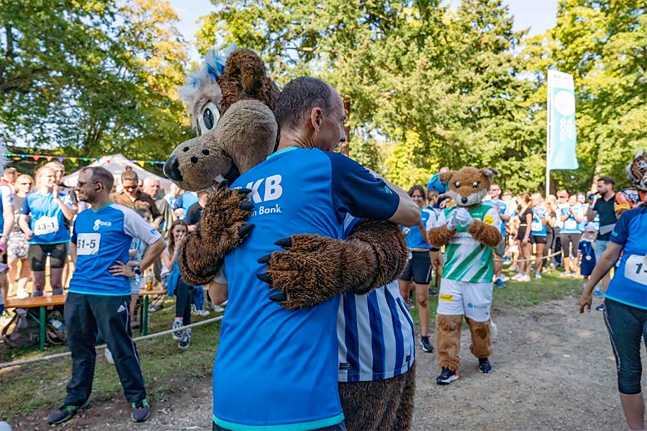 Mitarbeiter und das DKB Maskottchen umarmen sich