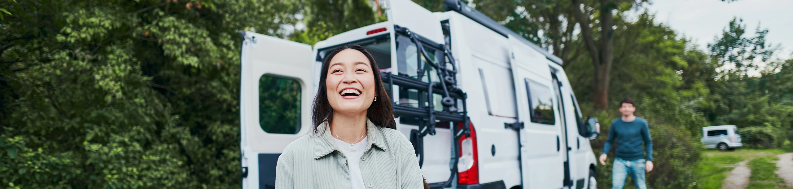 Eine lachende Frau steht vor einem Wohnmobil.