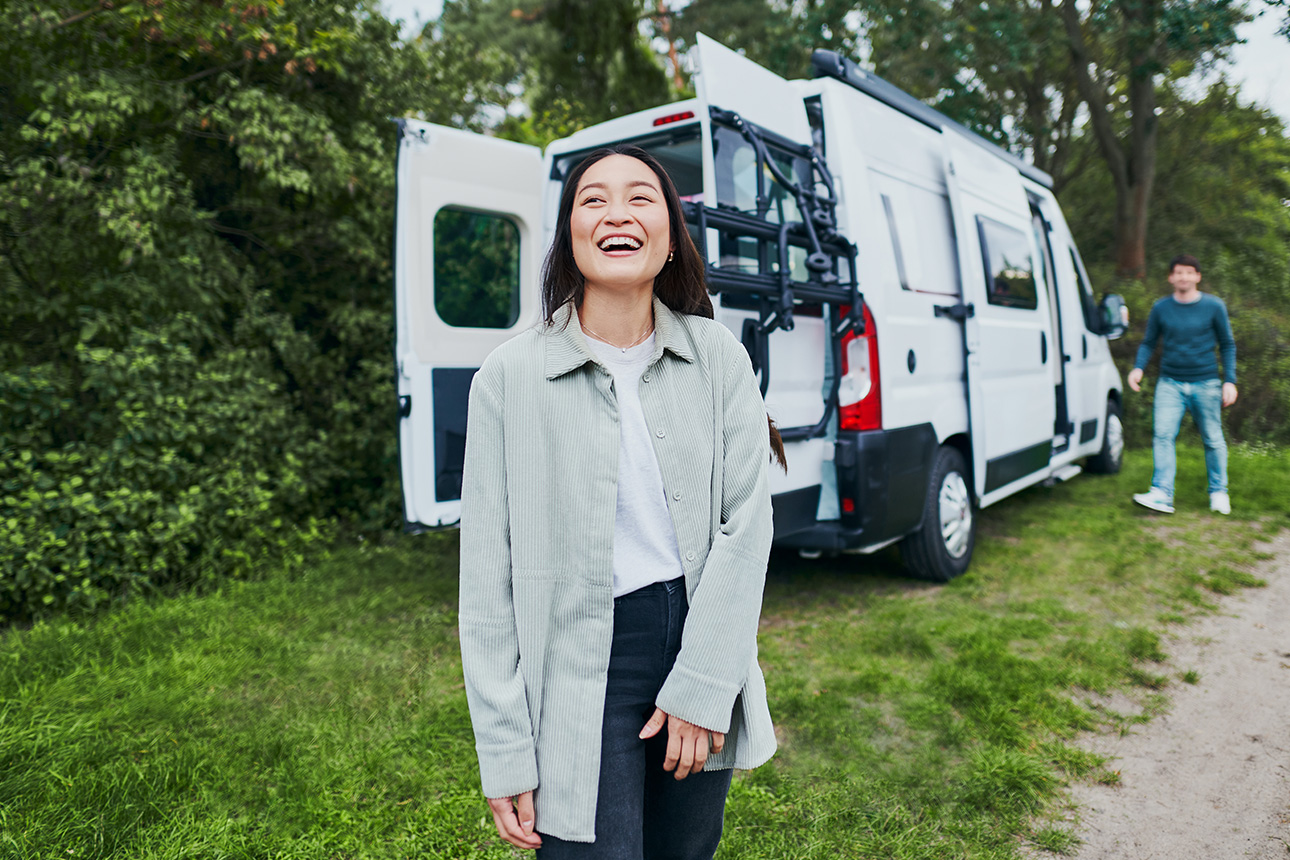 Eine lachende Frau vor einem Wohnmobil.