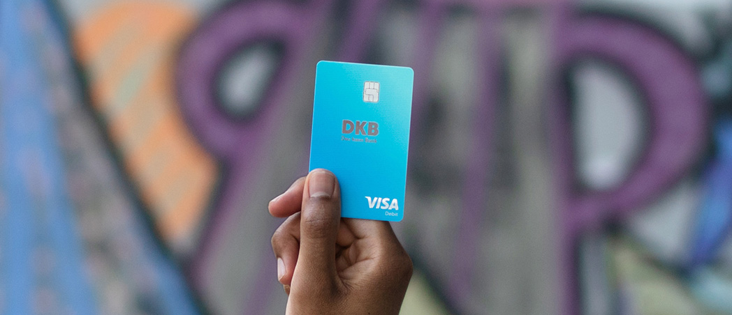 Hand hält Visa Debitkarte vor Wand mit Graffiti
 
