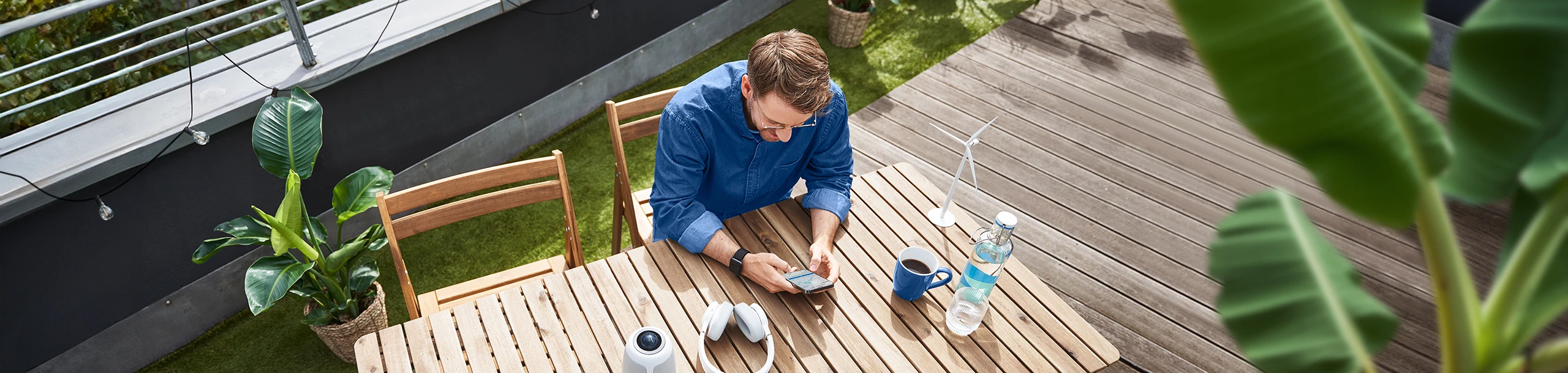 Ein Mann sitzt mit Smartphone in der Hand auf einer Terrasse.