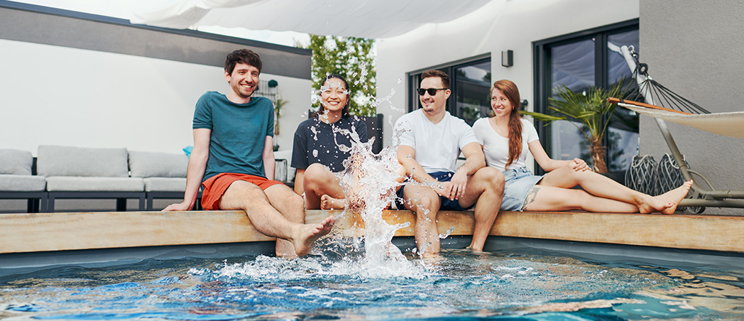 Vier Personen sitzen an einem Pool und spitzen mit Wasser.