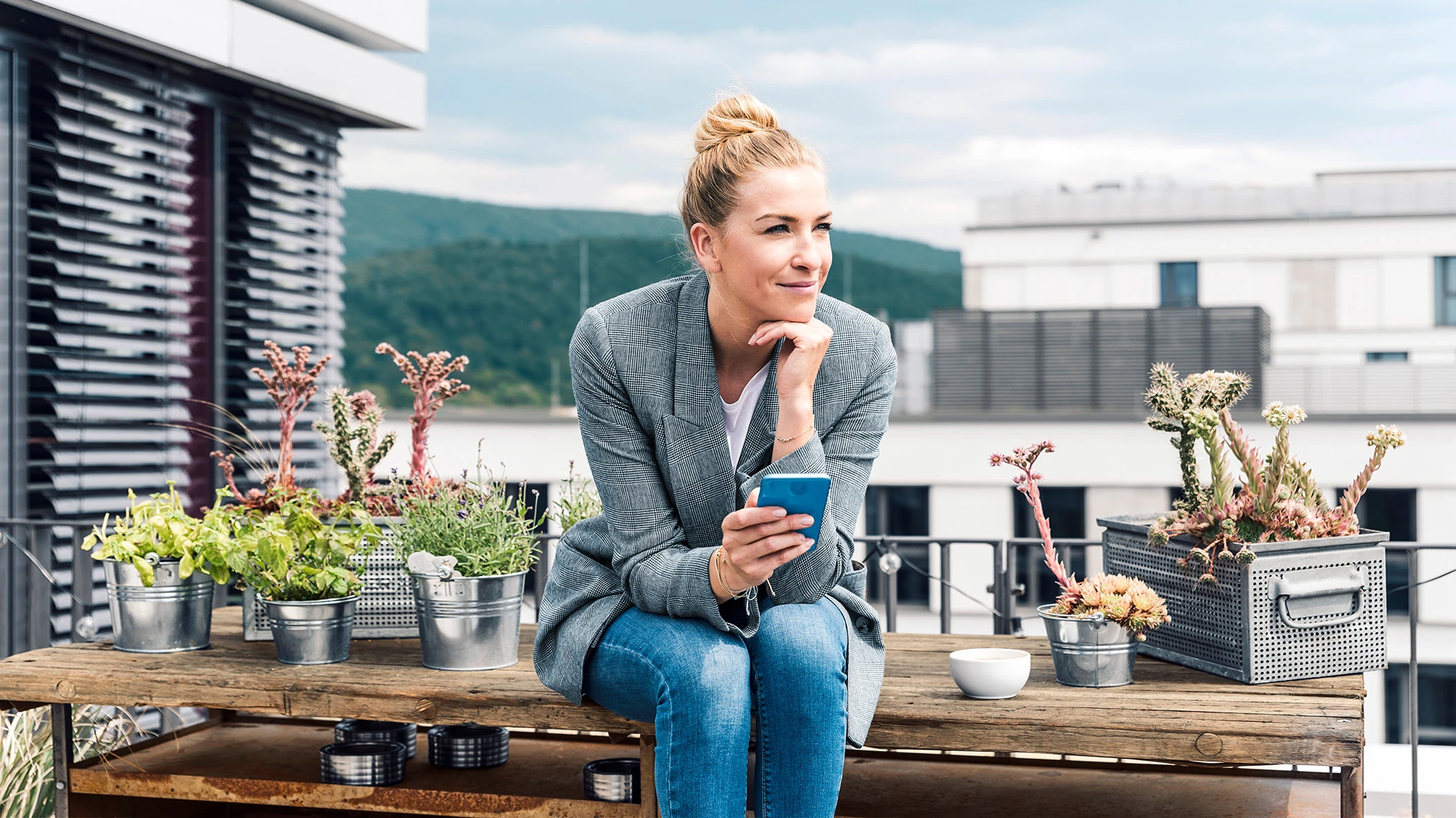 Eine Frau sitzt mit einem Handy auf einer Terrasse.