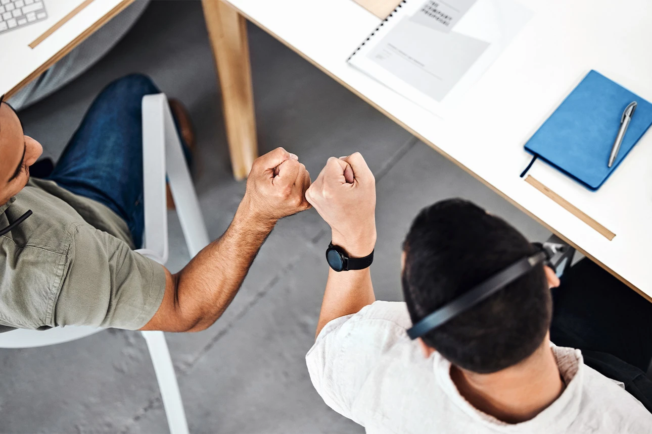 Zwei Menschen an Schreibtisch geben sich Fist Bump