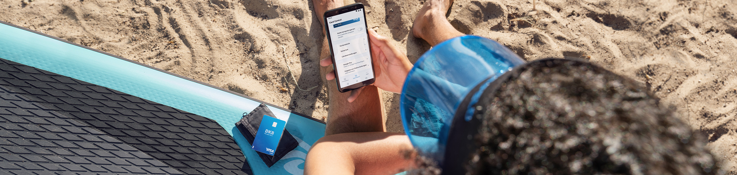 Person mit Smartphone und DKB Visa Kreditkarte am Strand