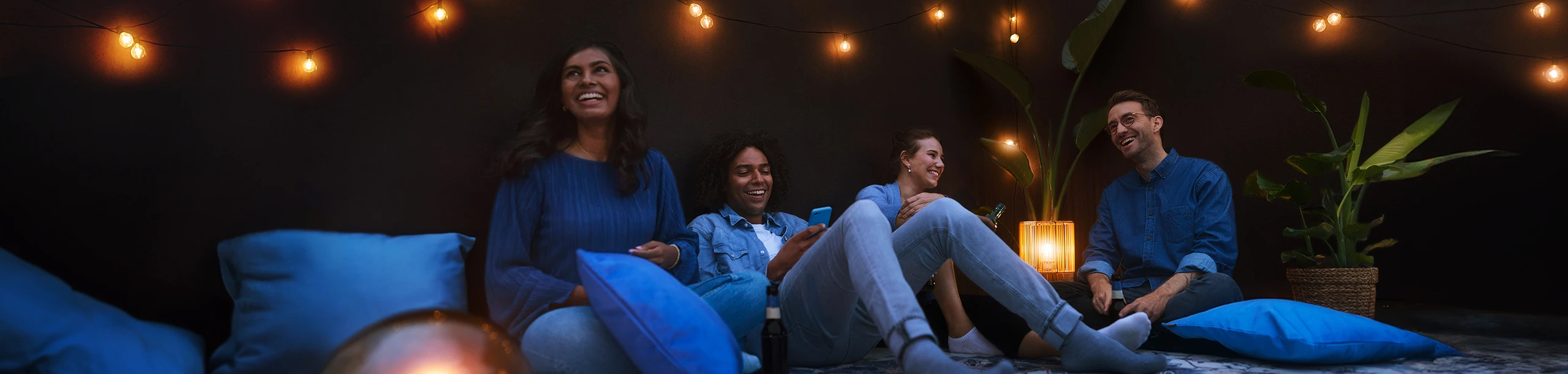 Gruppe junger Leute sitzt entspannt auf Dachterrasse im Dämmerlicht