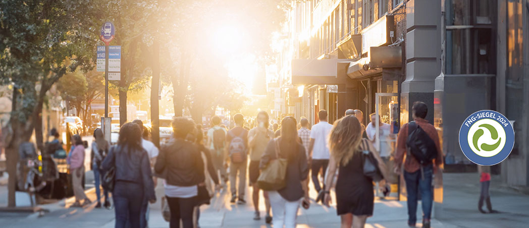 Eine sonnige und belebte Einkaufsstraße mit vielen Menschen.