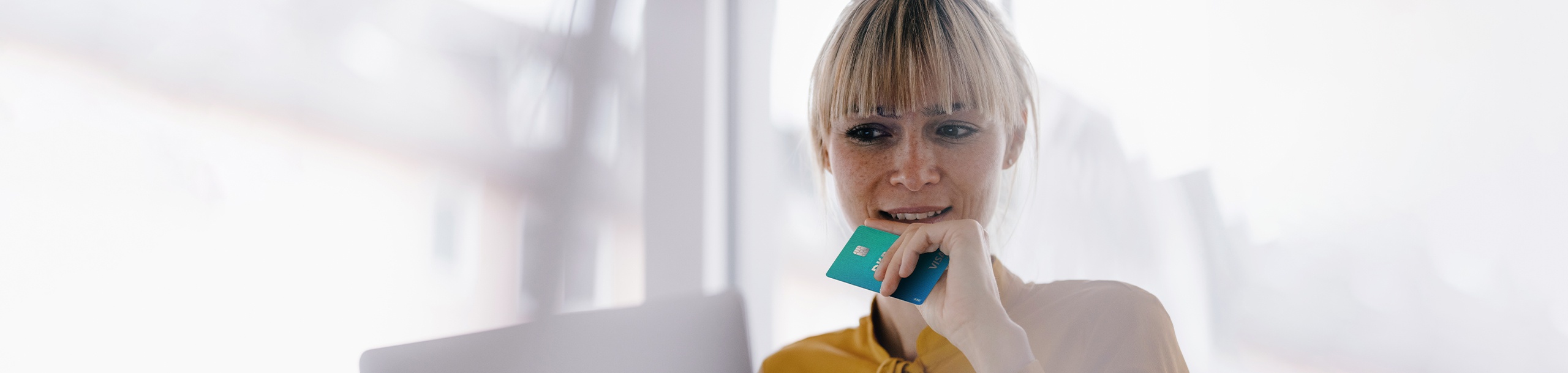 Frau hält Visa Debitkarte am Laptop sitzend