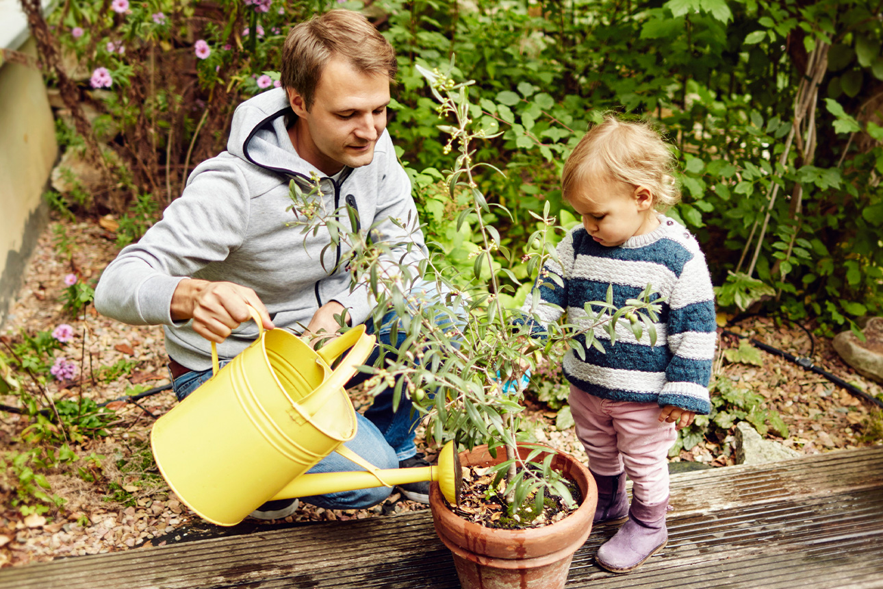 Mann mit Kind gießt Pflanze