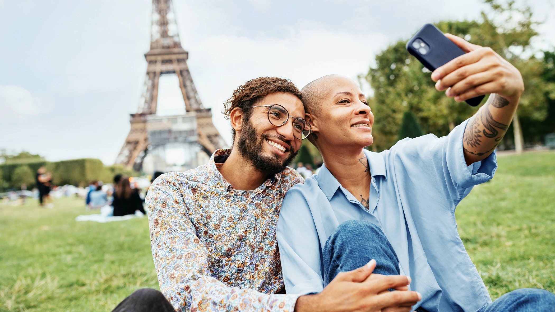 Ein Pärchen sitzt vor dem Eifelturm in Paris und macht ein Selfie.