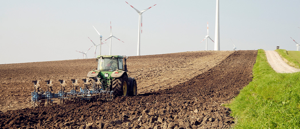 Traktor pflügt Acker, Windkraftanlagen im Hintergrund