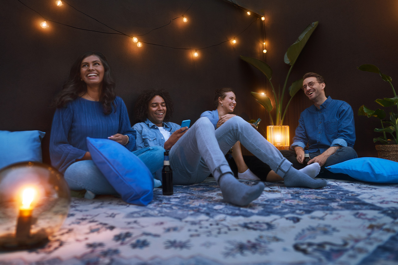 Gruppe junger Leute sitzt entspannt auf Dachterrasse im Dämmerlicht