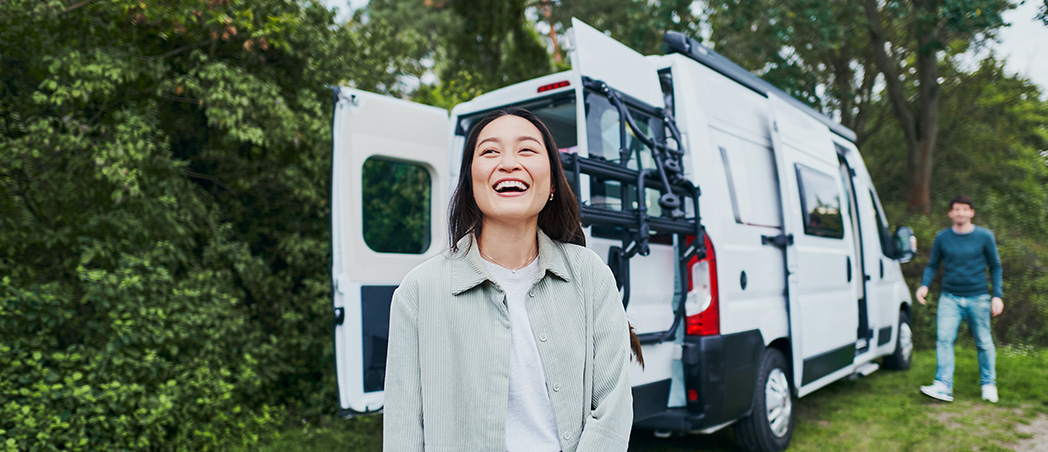 Eine lachende Frau steht vor einem Wohnmobil.