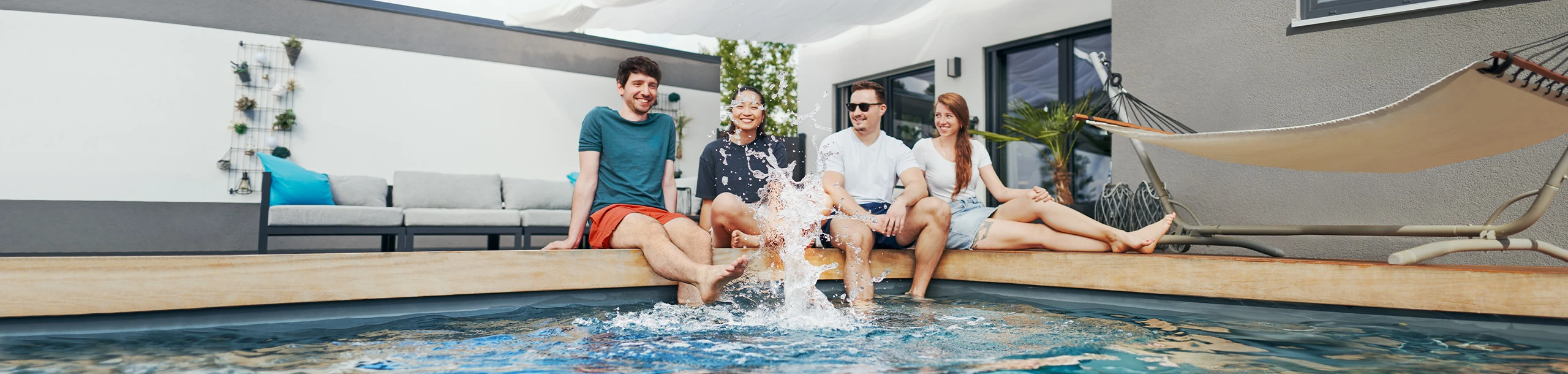 Vier Personen sitzen an einem Pool und spitzen mit Wasser.