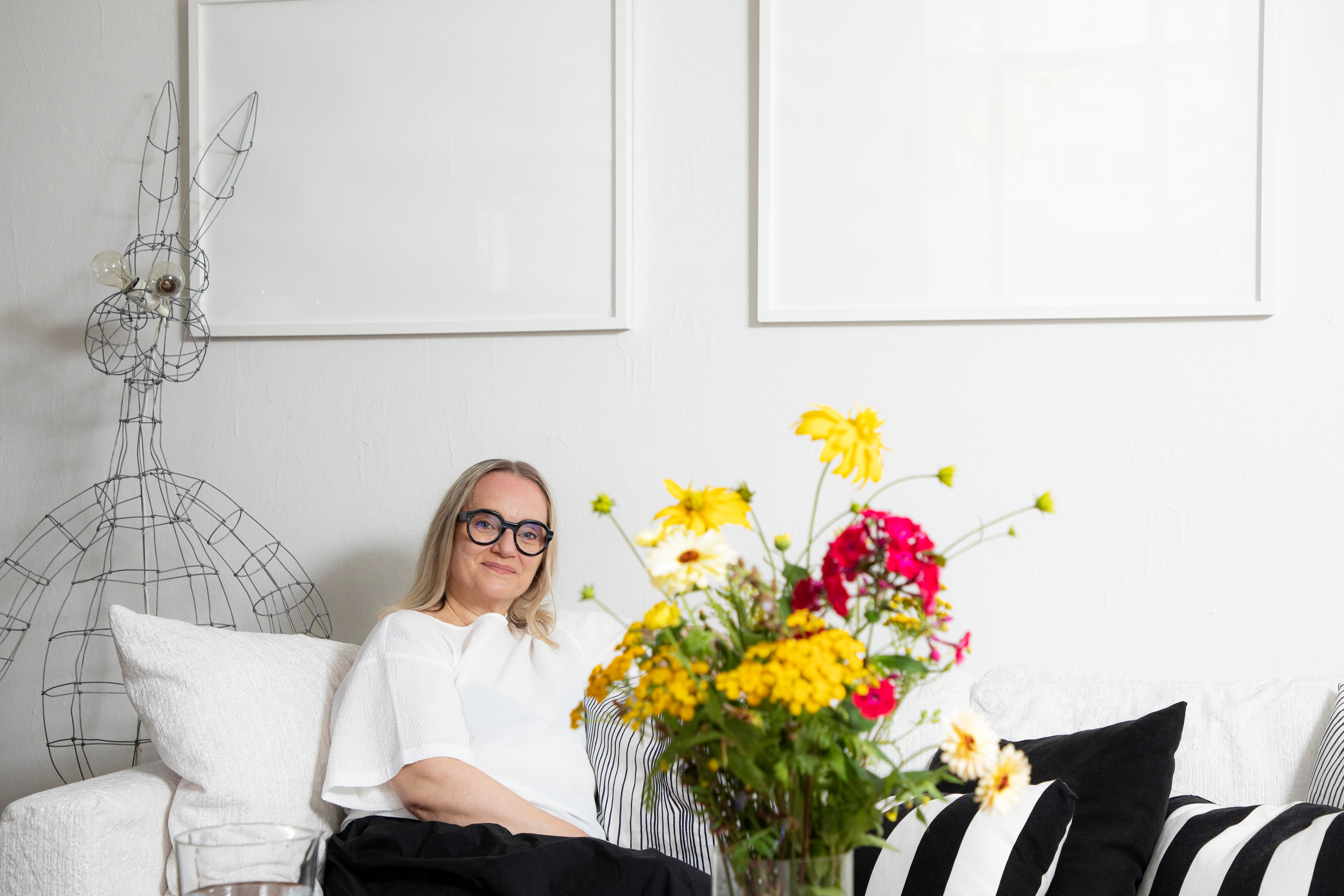 Helena Hietanen istuu sohvalla, etualalla kukkakimppu