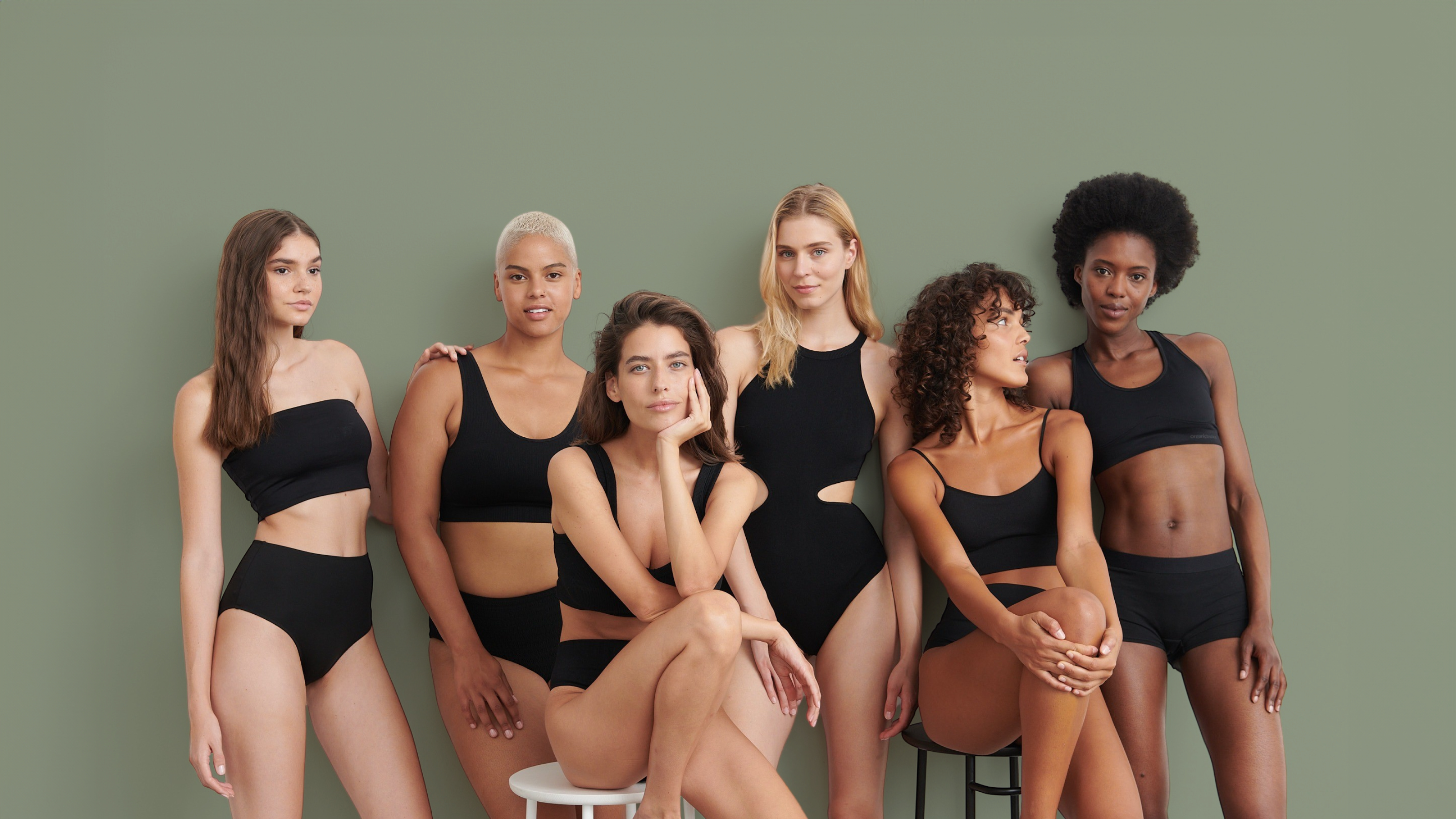 Siyah, sportif bikiniler giymiş, oturur ve ayakta durur konumda altı kadından oluşan bir grup.