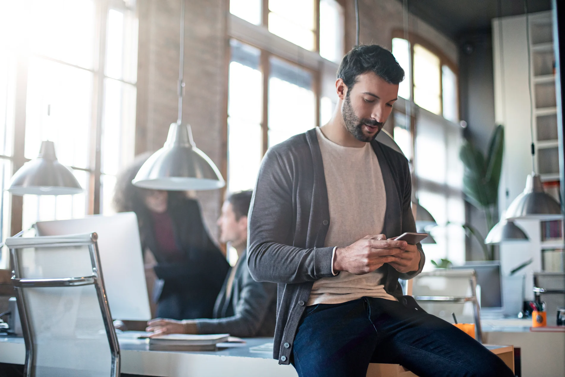 A person using their smartphone, casually sitting on a desk in a modern industrial-style office.