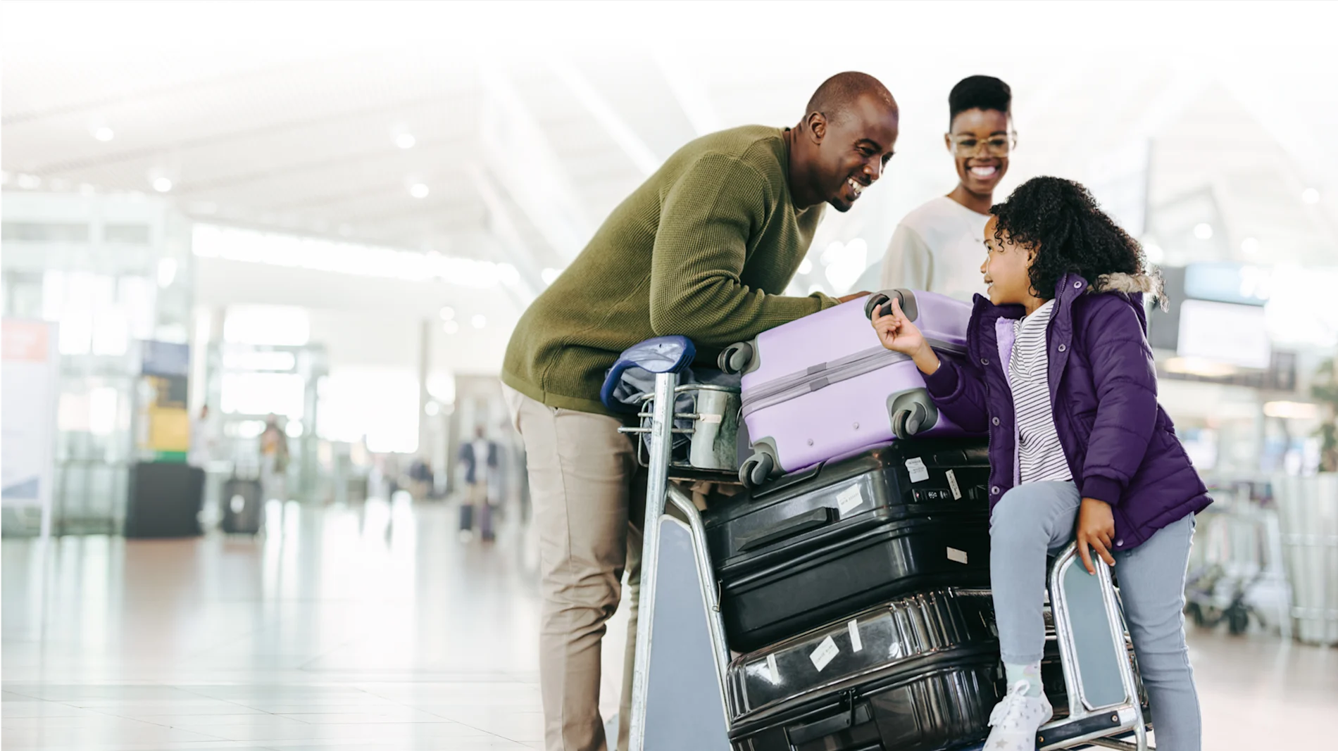 Une famille heureuse à l’aéroport avec ses bagages sur un chariot.