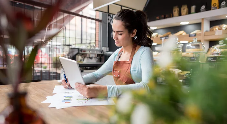 Small business owner reviewing documents and working on laptop in cafe.