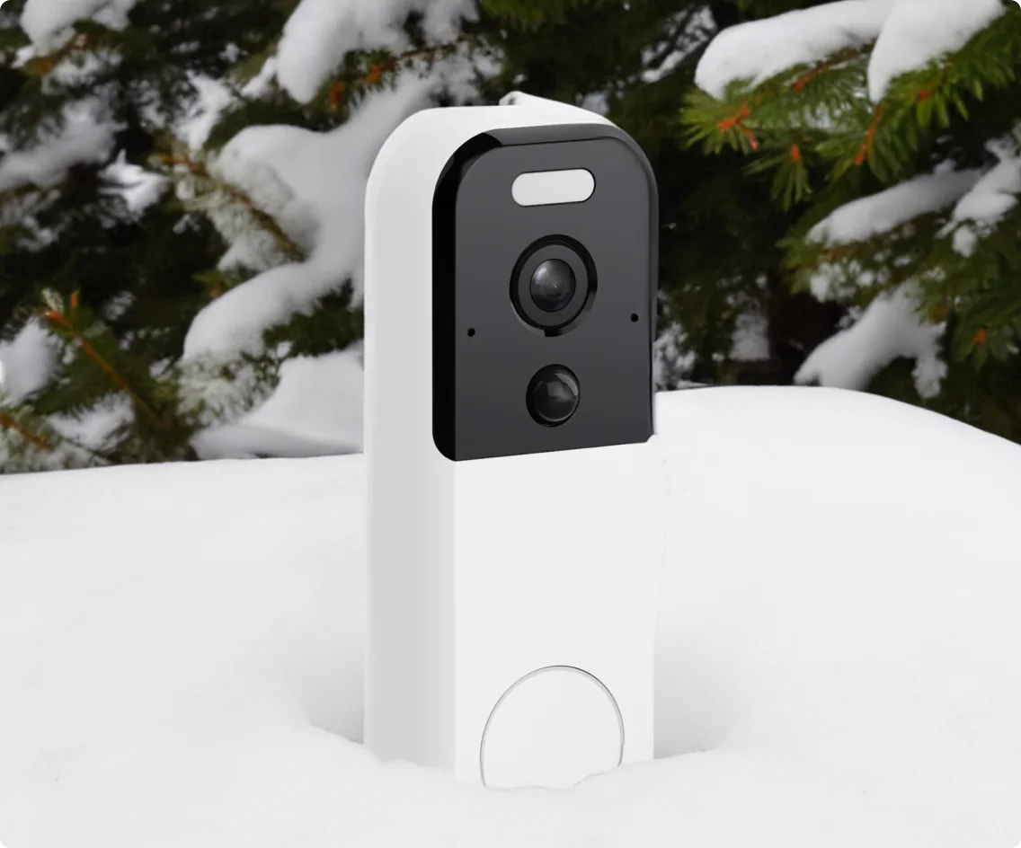 Doorbell camera sitting in large snowbank with some snow-covered tree branches in the background.