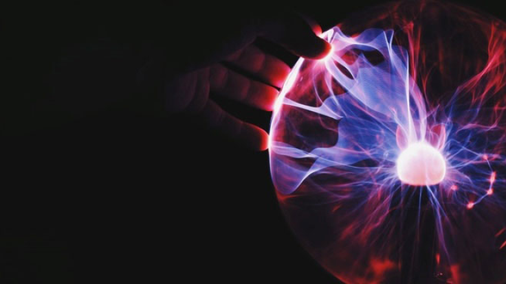 A person touches a plasma ball that’s lighting up the darkness.