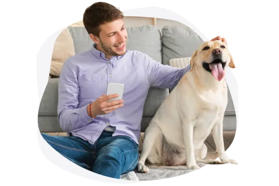 A man holding a smartphone sits petting a dog sitting beside him.