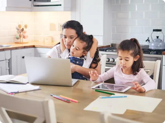 A family using a laptop and tablet at the kitchen table.