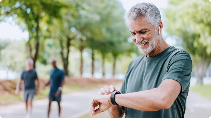 A man checking his smartwatch while standing on a tree-lined path in a park.