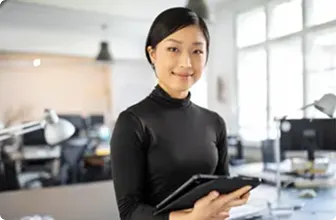 Professional woman holding a tablet and smiling in a bright, modern office, representing confidence and simplicity through SD-WAN solutions.