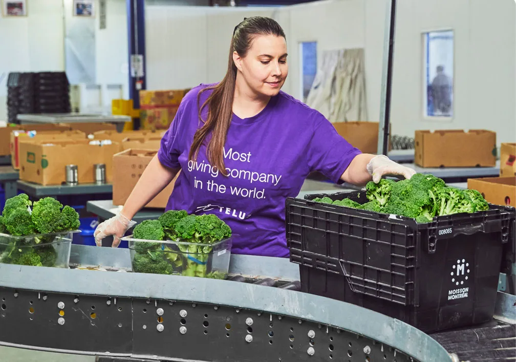 Une femme portant un t-shirt TELUS et évalue la qualité de légumes