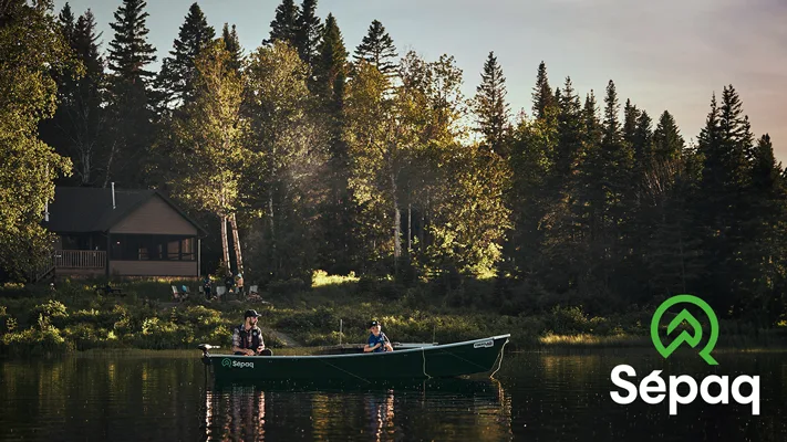 Two fishermen on a boat on a serene lake with the Sépaq logo displayed in the corner.