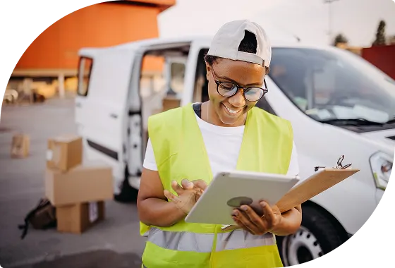 Delivery worker reviewing tablet near fleet vehicle at loading dock.