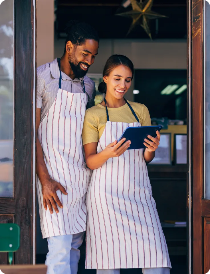 Propriétaires de petite entreprise à l’entrée de leur commerce consultant une tablette.