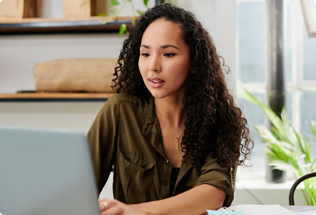 Woman works on a laptop at a desk in a home office.
