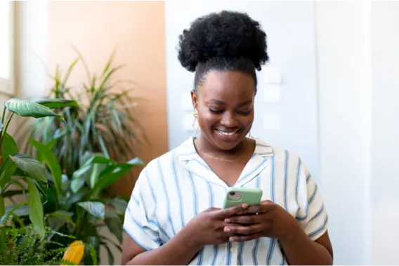 Smiling woman, standing beside plants, looking at her phone